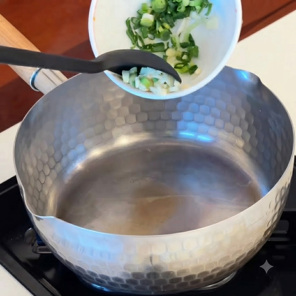 Lail émincé, les morceaux de kimchi rouge et les rondelles de saucisses versés dans une casserole chaude.