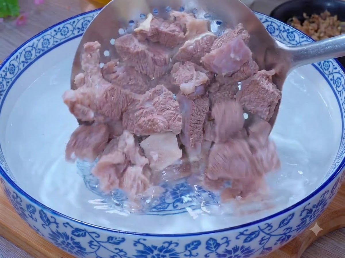 Des morceaux de bœuf blanchis nettoyés dans un bol deau chaude à laide dune écumoire.