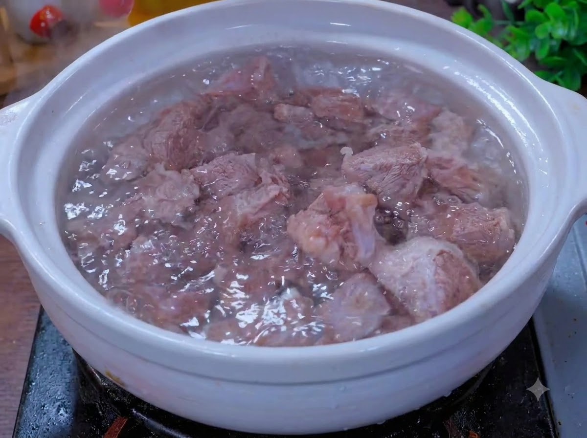 Des morceaux de bœuf mijotant dans une marmite en terre cuite blanche avec des aromates.