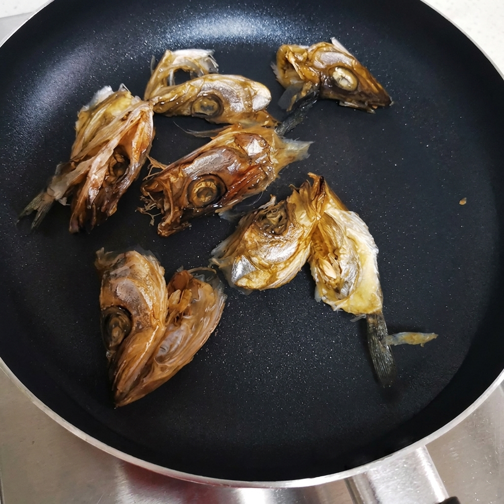 Têtes de poisson séché disposées dans une casserole plate avec de leau froide prêtes à être chauffées.