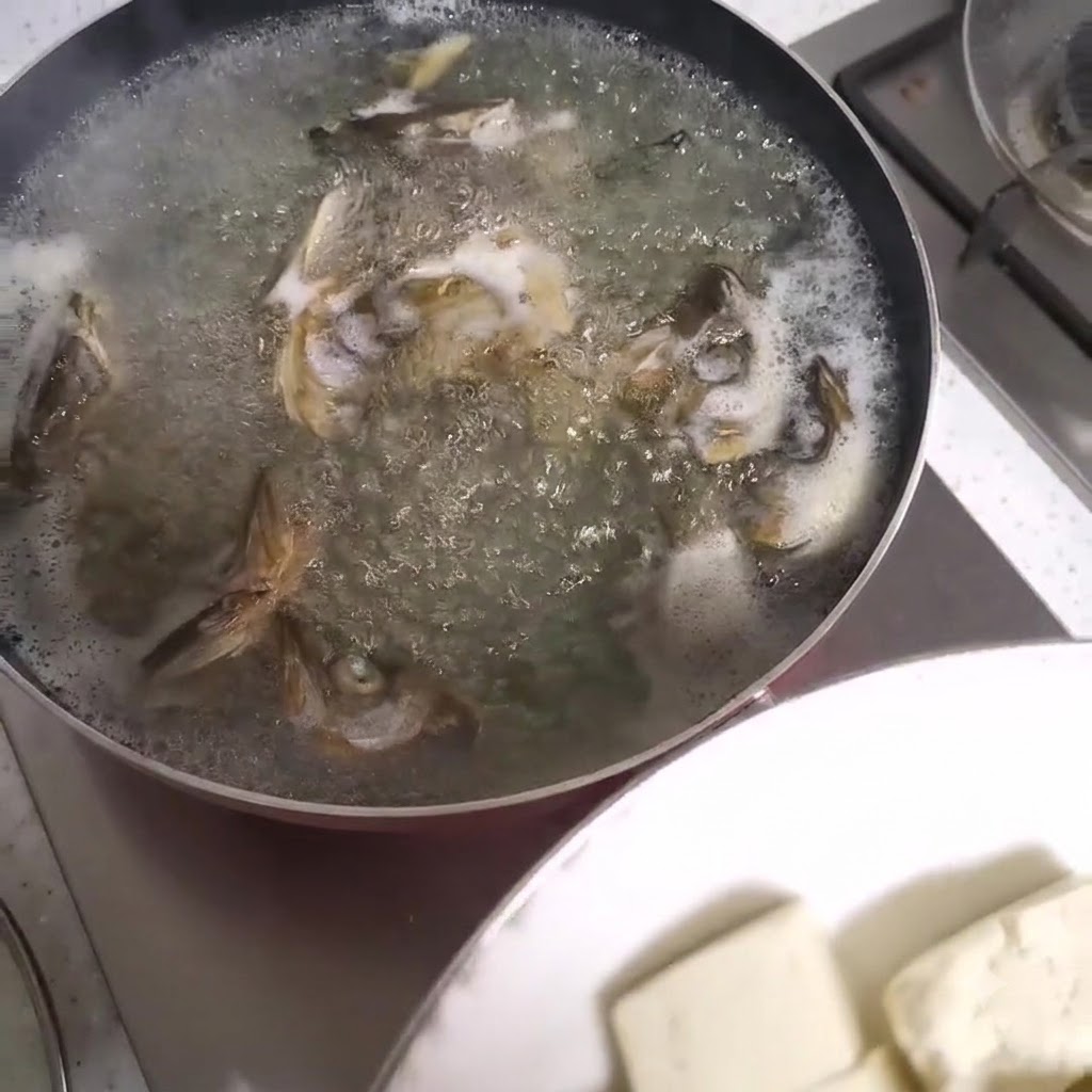 Cubes de tofu en train dêtre ajoutés dans une casserole bouillante de soupe de têtes de poisson.
