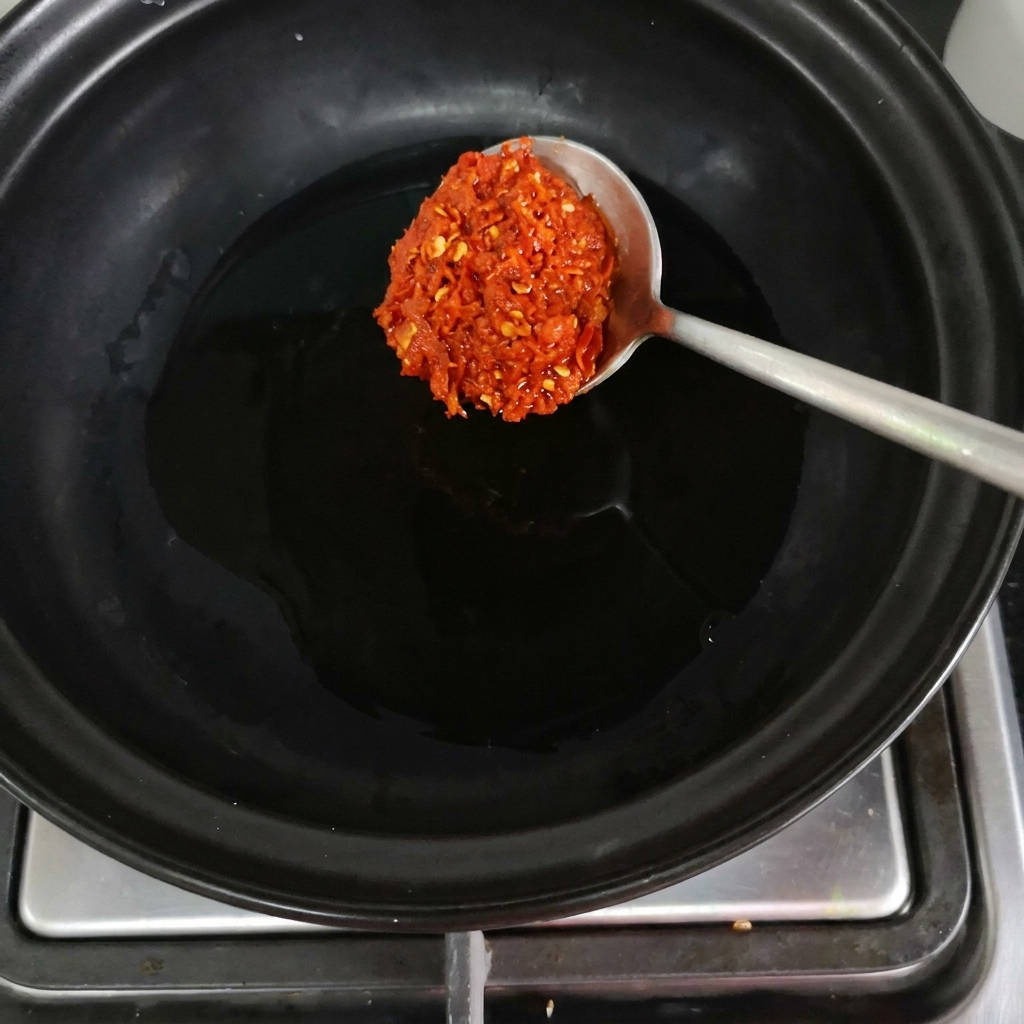 Une cuillerée de pâte de piment rouge déposée dans un caquelon noir sur le feu.