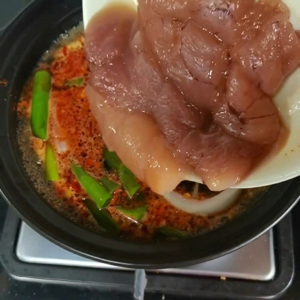 Des morceaux frais dœufs de colin transférés dune assiette vers une casserole de soupe frémissante avec des légumes verts.