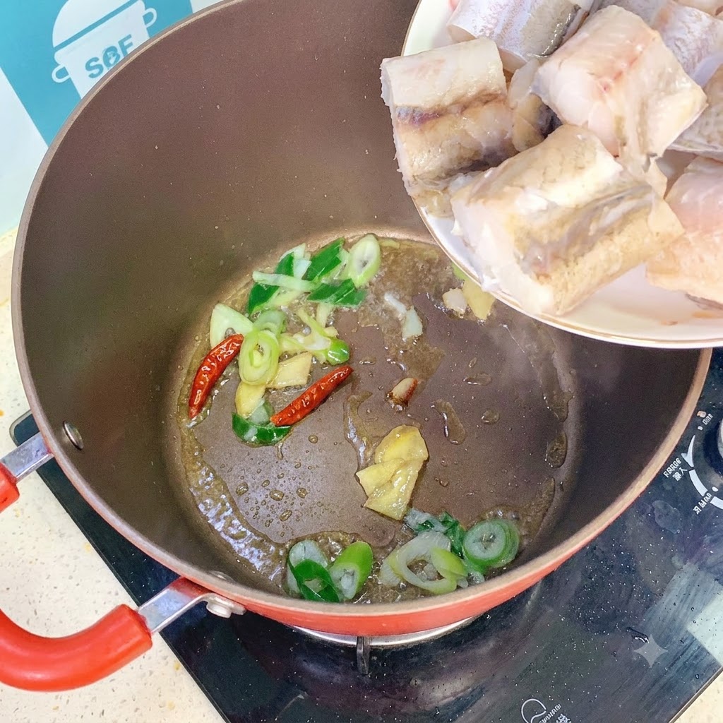 Des morceaux de poisson ajoutés dans la marmite contenant les aromates et les piments sautés.