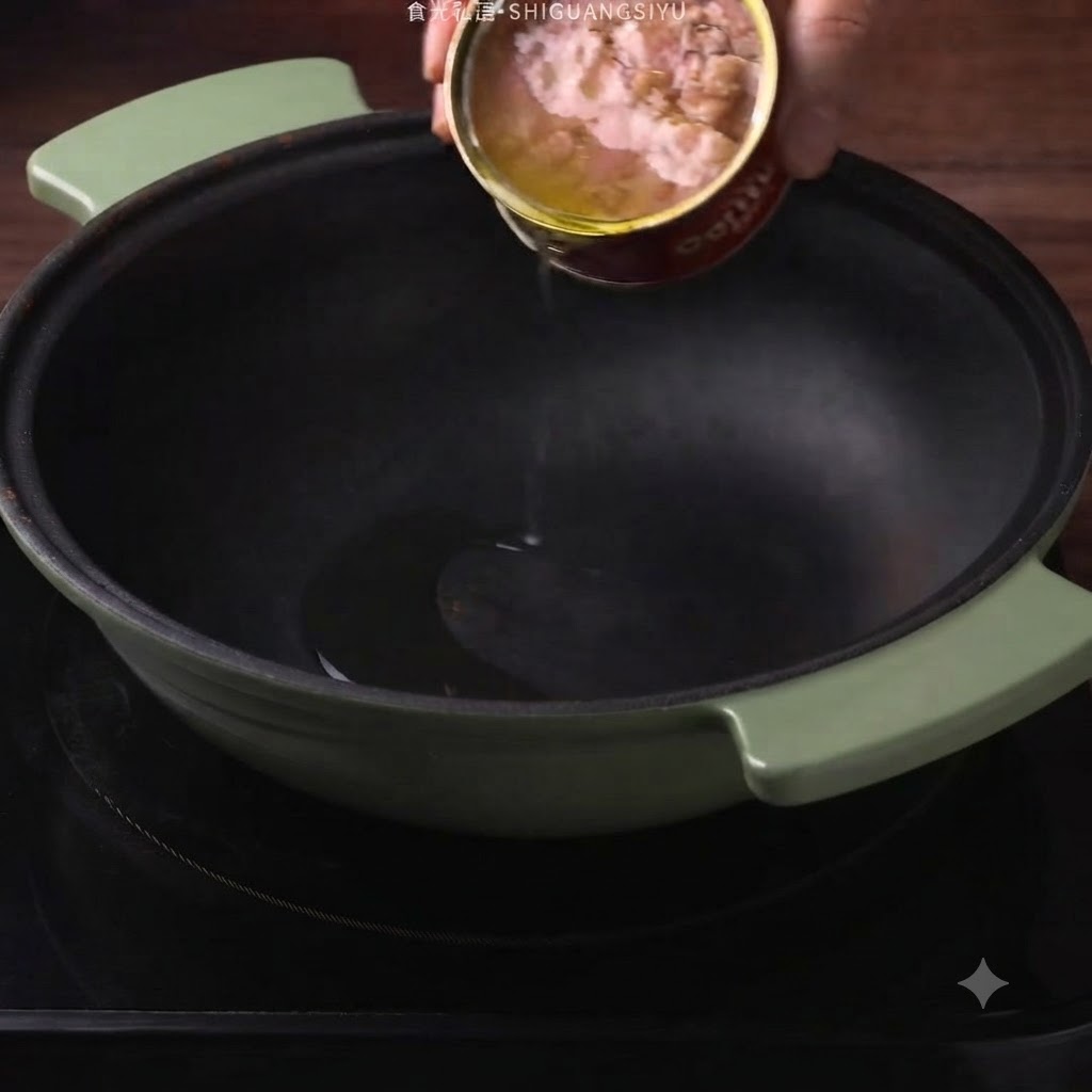 De lhuile de thon en conserve versée depuis une boîte dans une cocotte vert foncé.