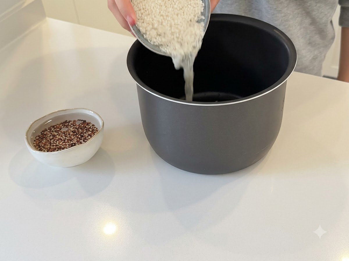 Mains versant du riz blanc dans une cuve de cuiseur à riz avec un petit bol de quinoa à côté.