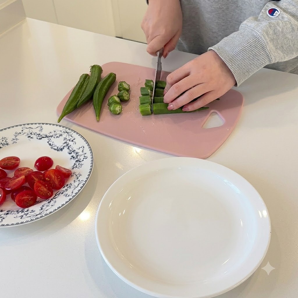 Mains coupant des gombos verts en petites rondelles sur une planche à découper rose.