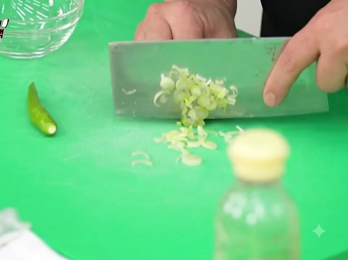 Des oignons verts, des piments Cheongyang et des oignons hachés finement sur une planche à découper verte avec un couteau de boucher.