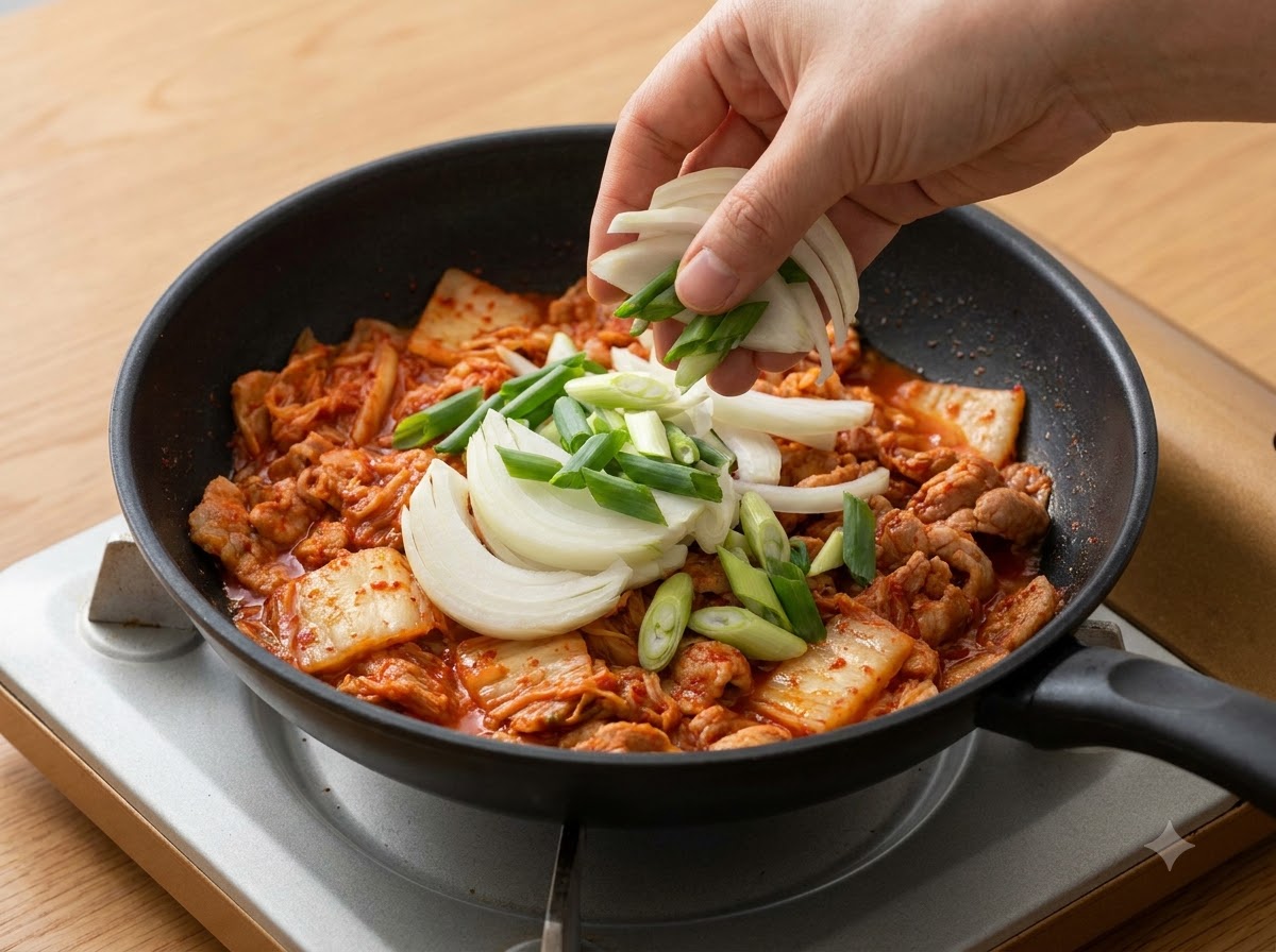 Des oignons tranchés et des oignons verts ajoutés dans la casserole par-dessus le kimchi.