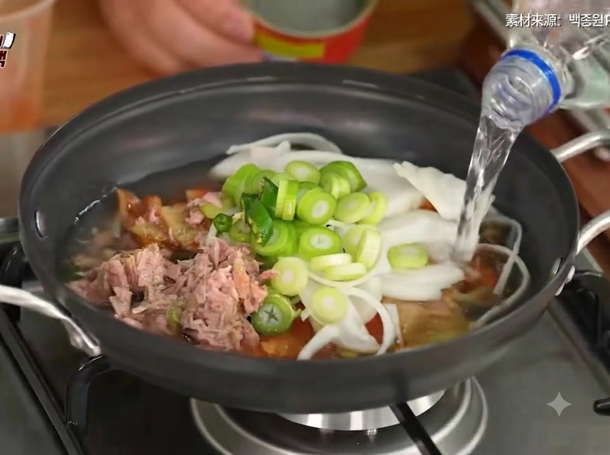 De leau versée dans la casserole contenant le kimchi, les légumes et le thon.