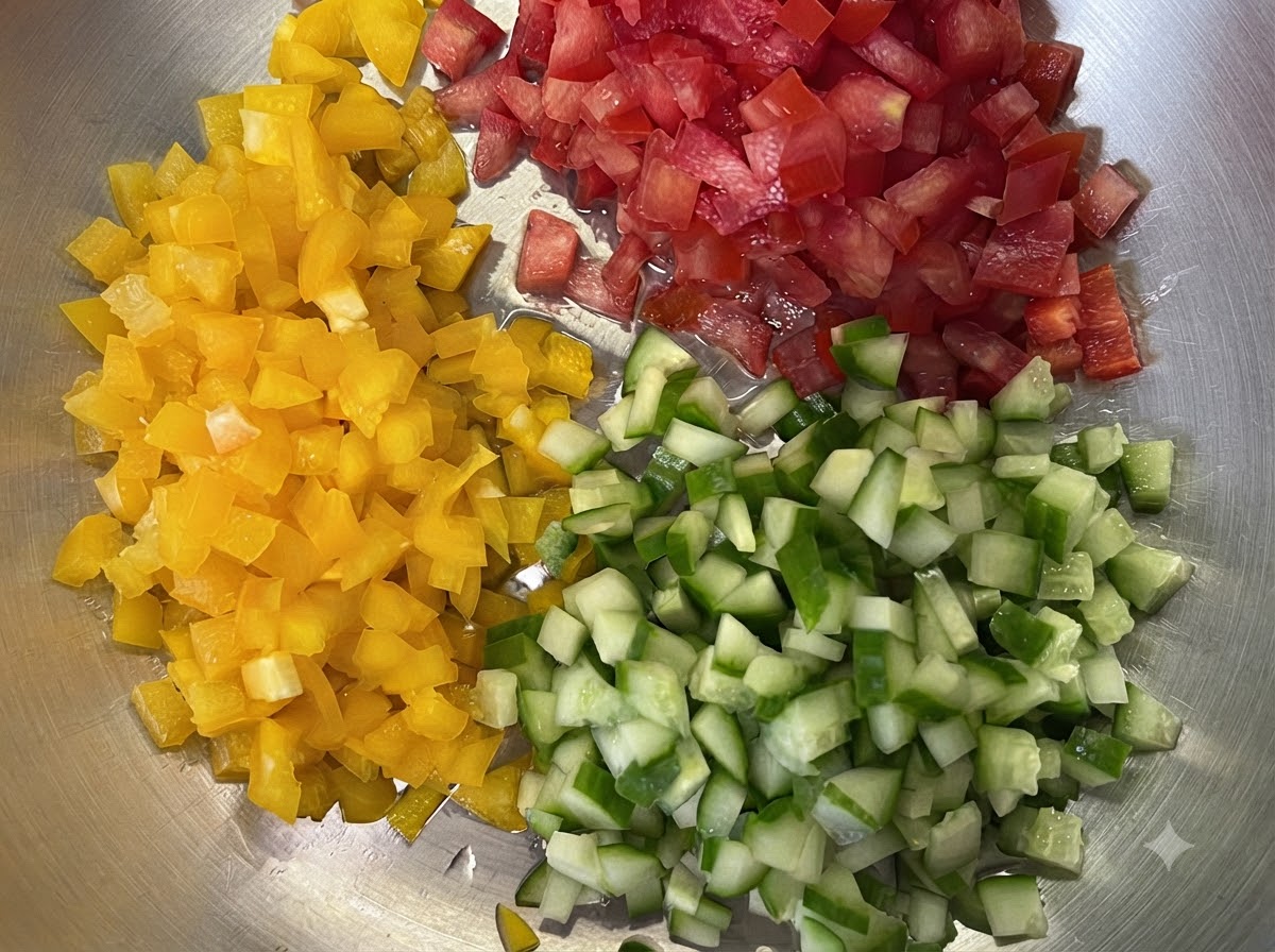 Poivrons jaunes, tomates rouges et concombres verts finement coupés en petits cubes sur un plateau.