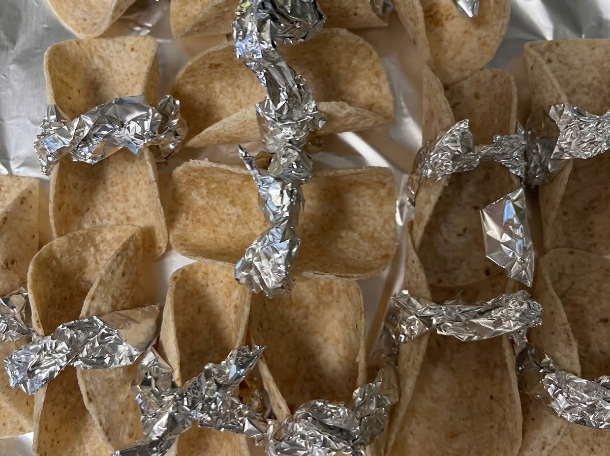 Petites tortillas disposées et fixées avec des morceaux de papier aluminium sur une plaque de cuisson prêtes pour le four.