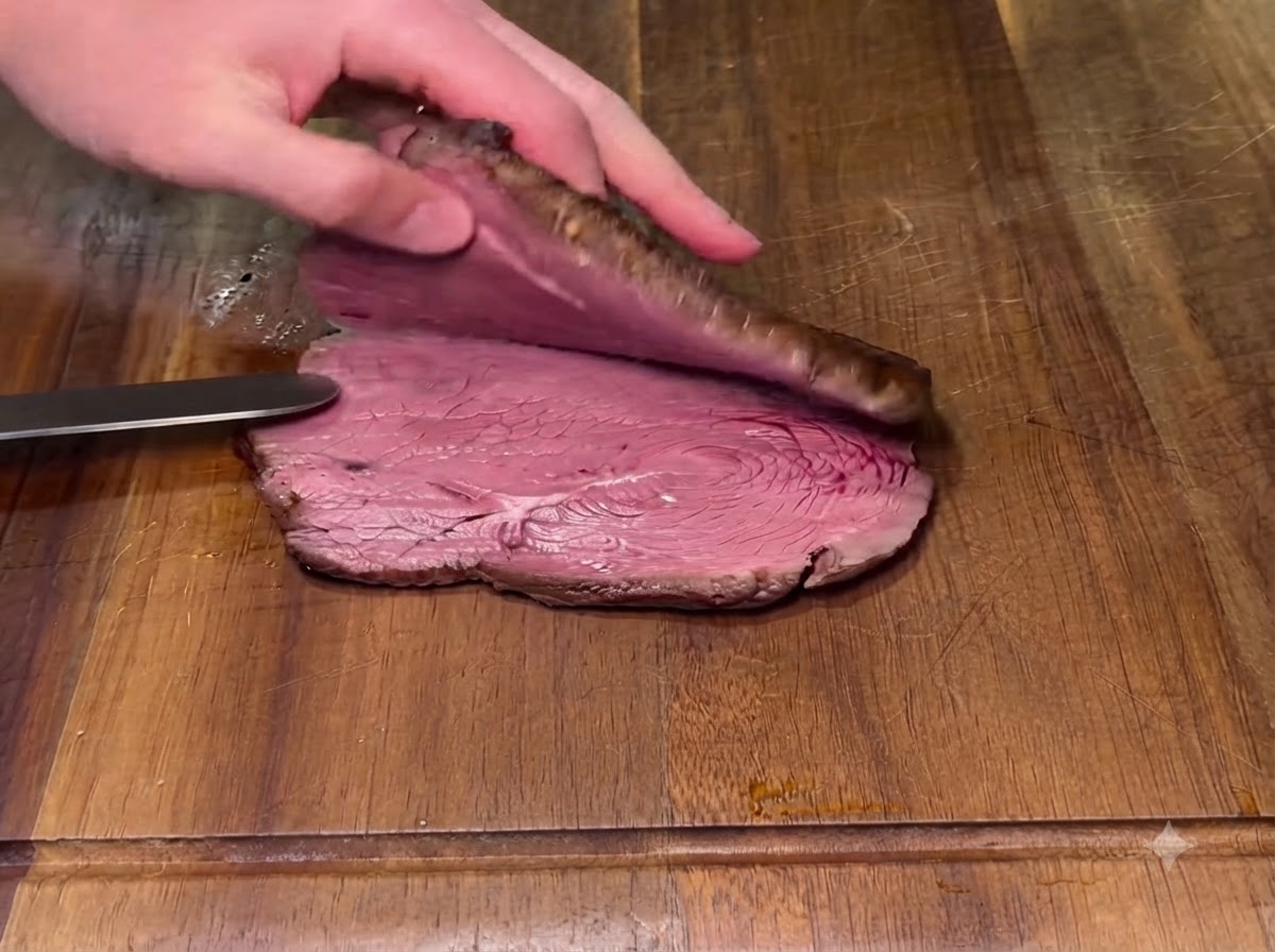 Un steak cuit coupé en deux horizontalement sur une planche à découper en bois avec un couteau.