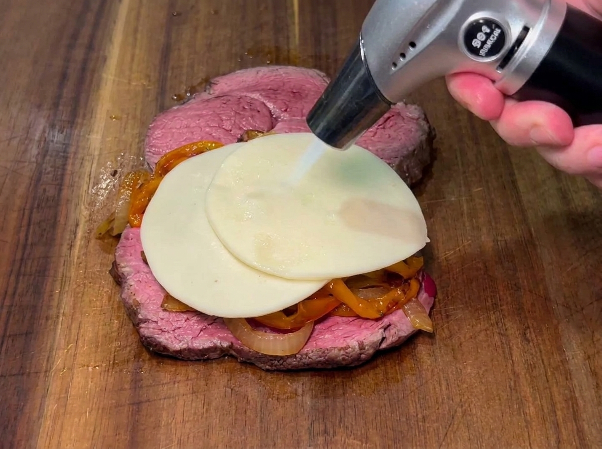 Une tranche de fromage fondue avec un chalumeau sur les poivrons et les oignons dun steak.