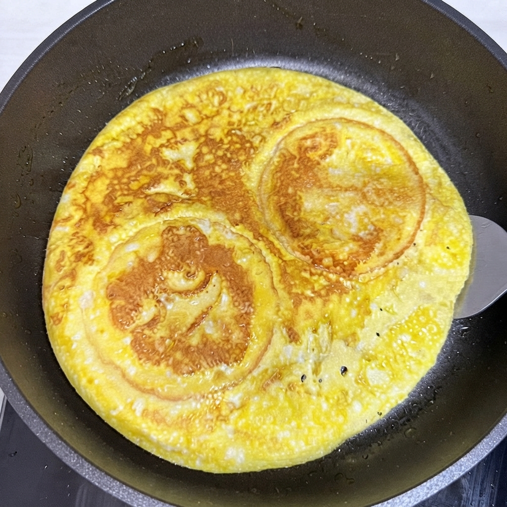 Une spatule retournant une couche ronde dœuf cuit et de pain à burger à lintérieur dune poêle à frire.
