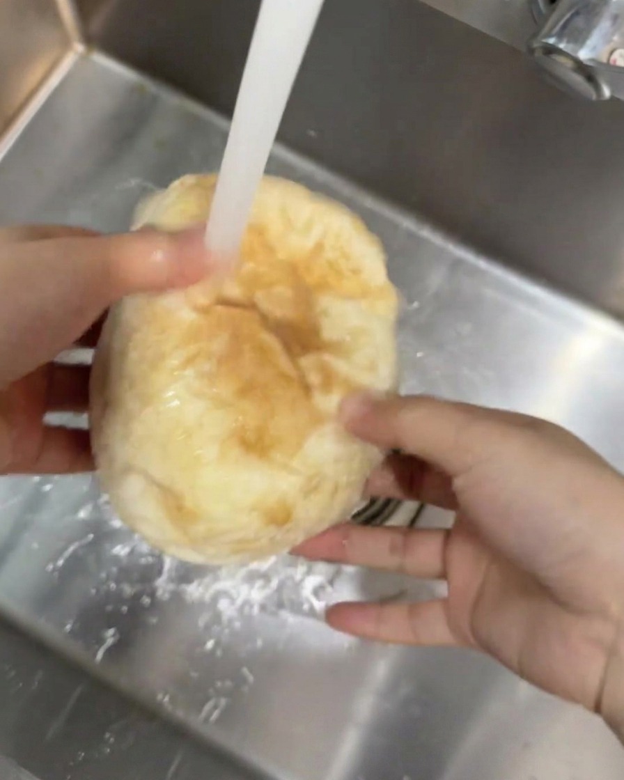 Un pain ciabatta rond tenu sous un filet deau courante dans un évier de cuisine.