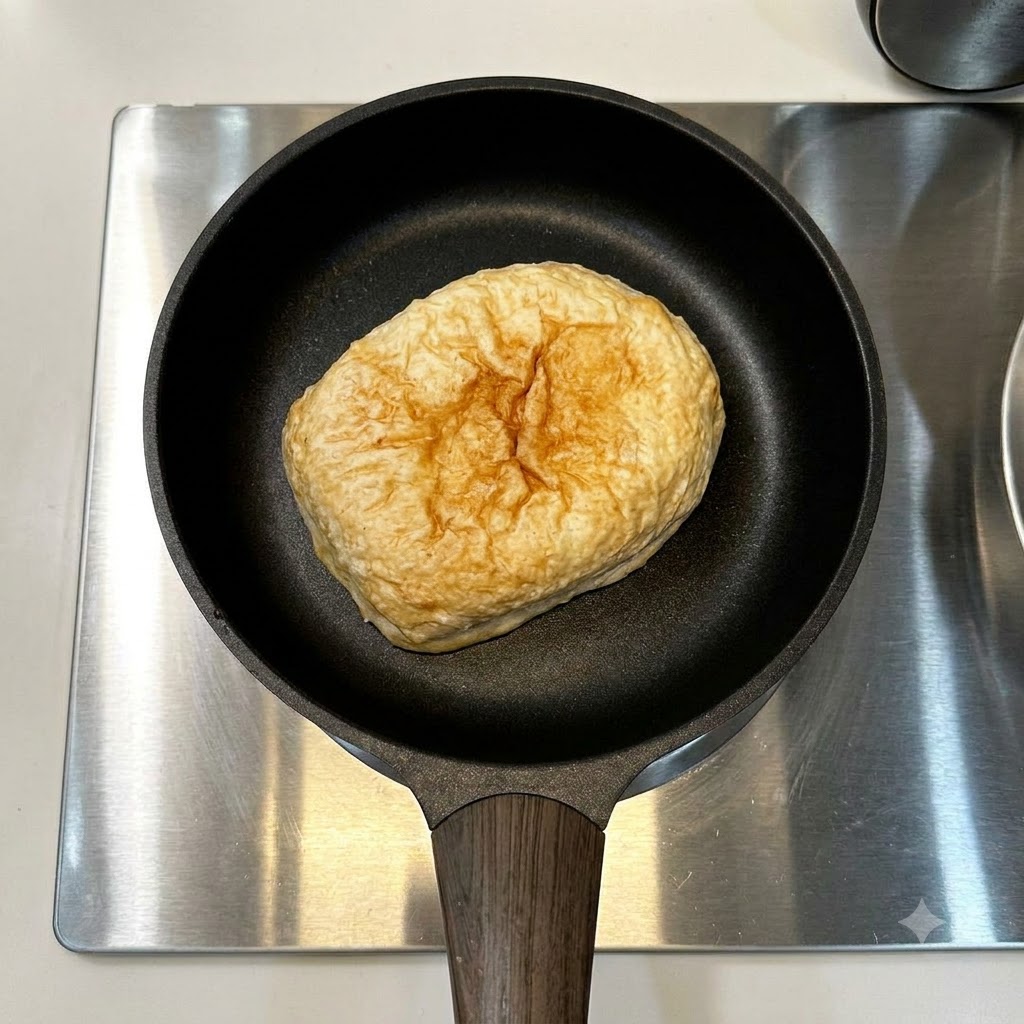Pain ciabatta et une seule saucisse reposant dans une poêle noire sur une cuisinière en acier inoxydable.