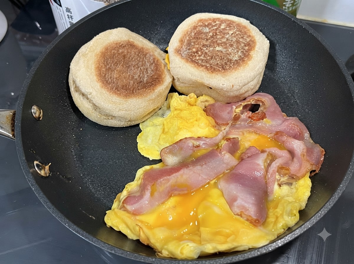 Œufs brouillés dans une poêle avec des tranches de bacon et des muffins anglais posés sur le côté.