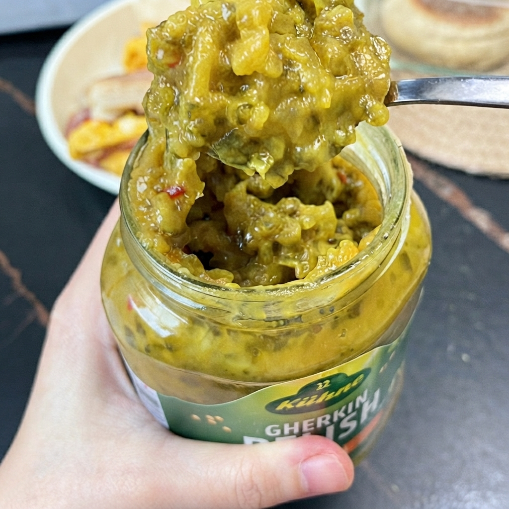 Une cuillérée de relish de cornichons vert vif sortie dun bocal en verre à laide dune petite cuillère.