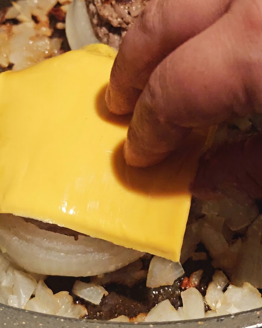 Une tranche de fromage jaune posée sur le dessus dune rondelle doignon farcie de viande cuite dans la poêle.