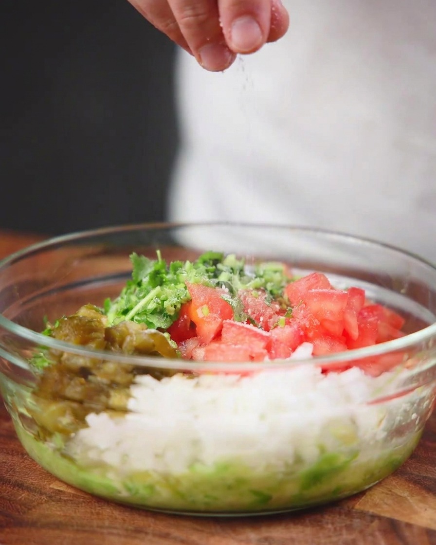 Du sel de mer saupoudré par le dessus dans un bol en verre transparent rempli de tomates, doignons, de poivrons et dherbes hachés.