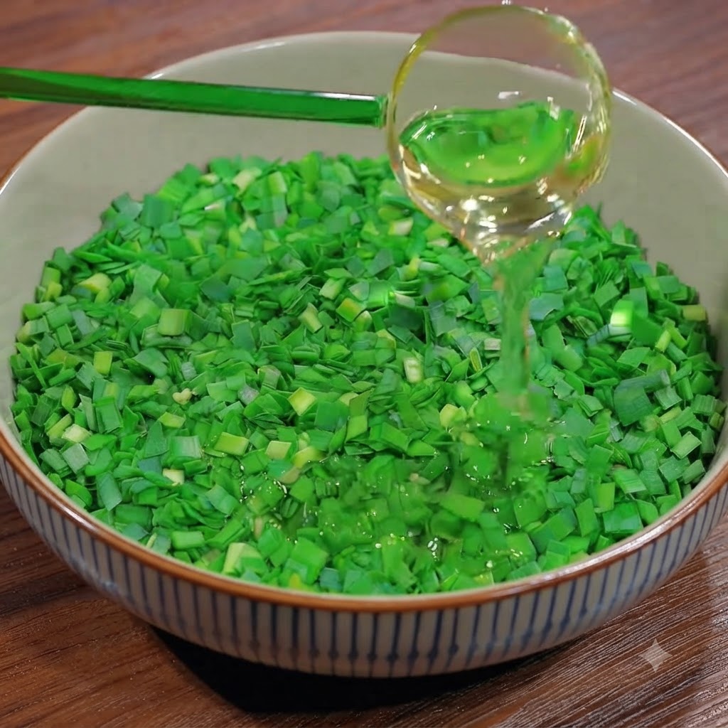 Une louche versant de lhuile de cuisson sur un bol rempli de ciboulette verte fraîchement hachée.