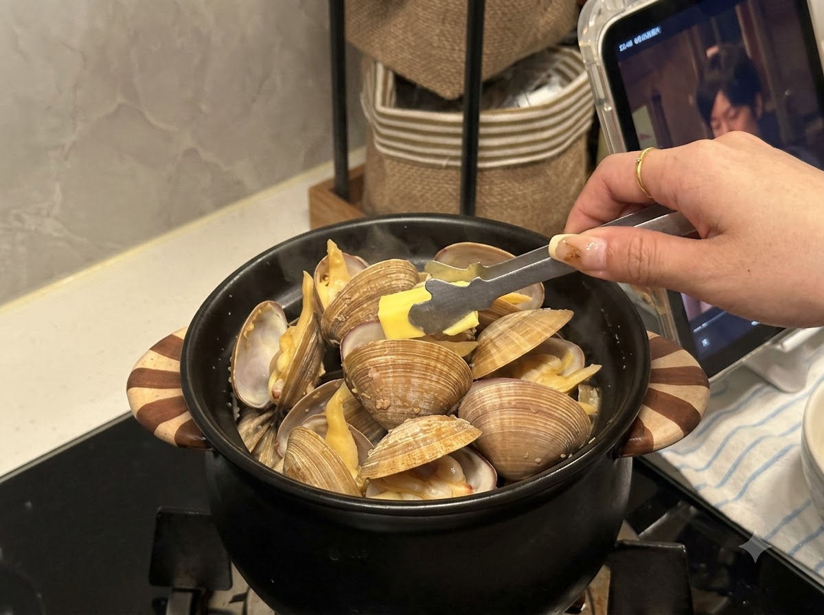 Un petit morceau de beurre placé à laide de pinces dans un pot noir rempli de palourdes ouvertes.