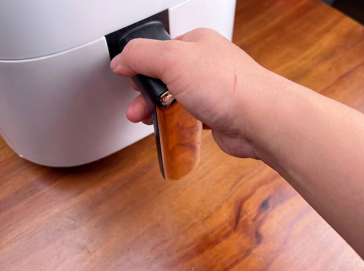 Une personne tenant la poignée dun air fryer blanc, sur le point de glisser le panier à lintérieur.