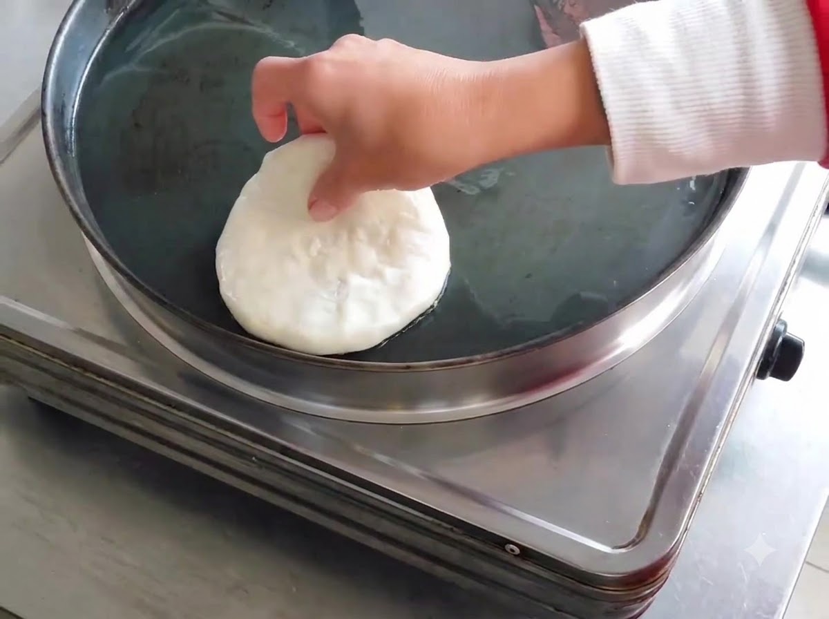 Une galette de viande crue déposée dans une poêle électrique plate et huilée.