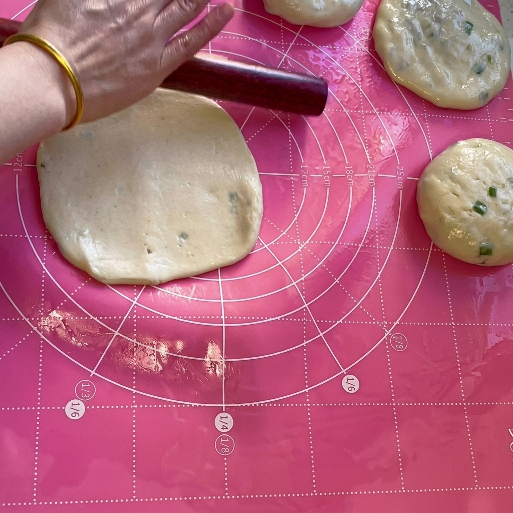 Un rouleau à pâtisserie en bois aplatissant une portion de pâte en un cercle fin sur un tapis rose.