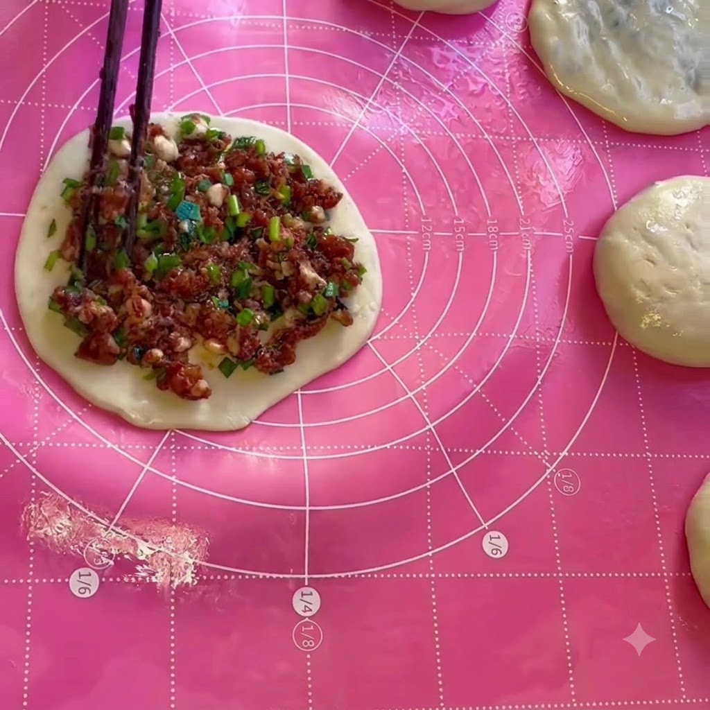 Farce de viande et ciboulette étalée uniformément sur une feuille de pâte ronde à laide de baguettes.