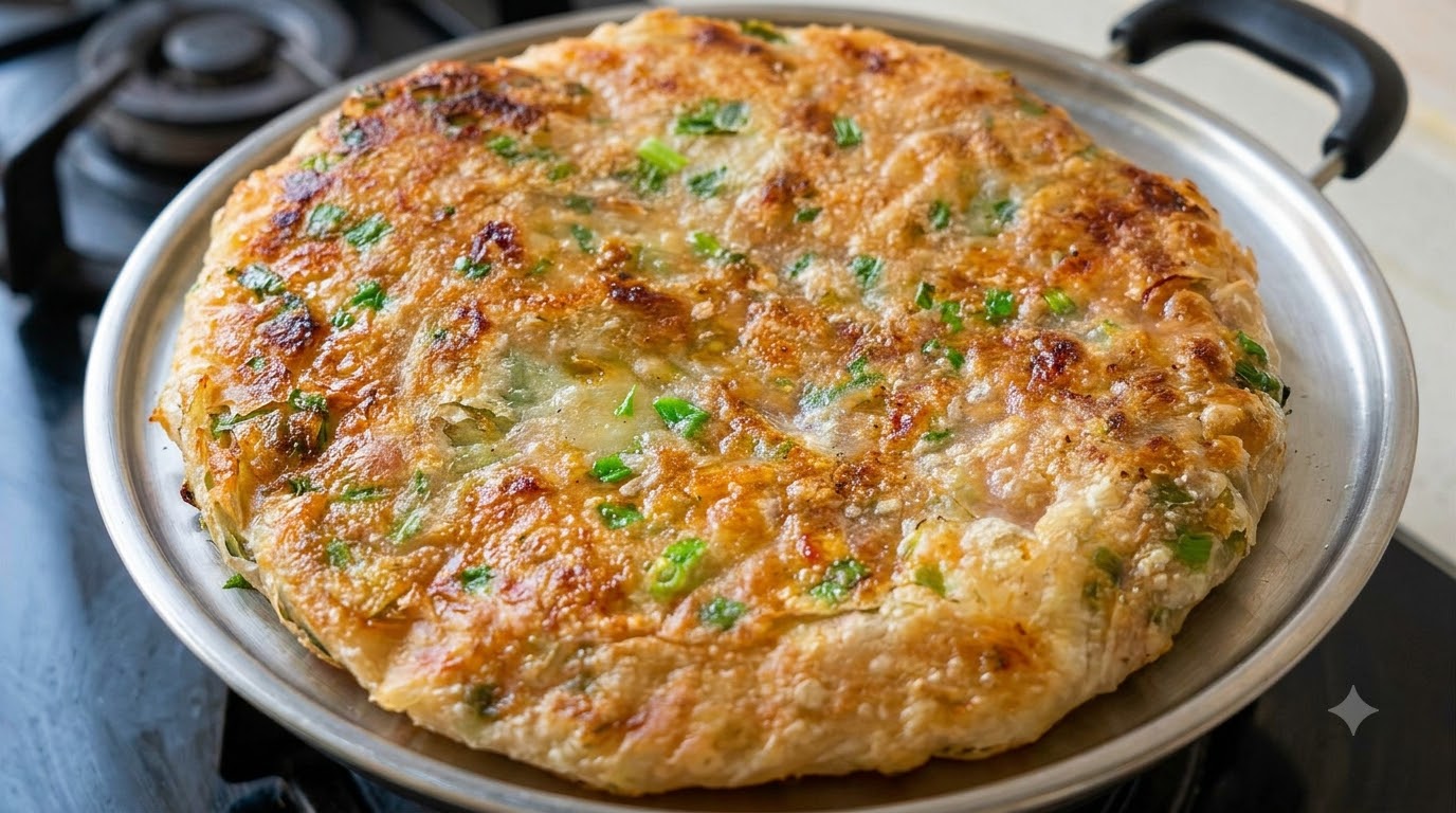 Une galette croustillante à la viande et aux oignons verts dorée dans une poêle, révélant une croûte feuilletée parsemée de ciboule hachée.