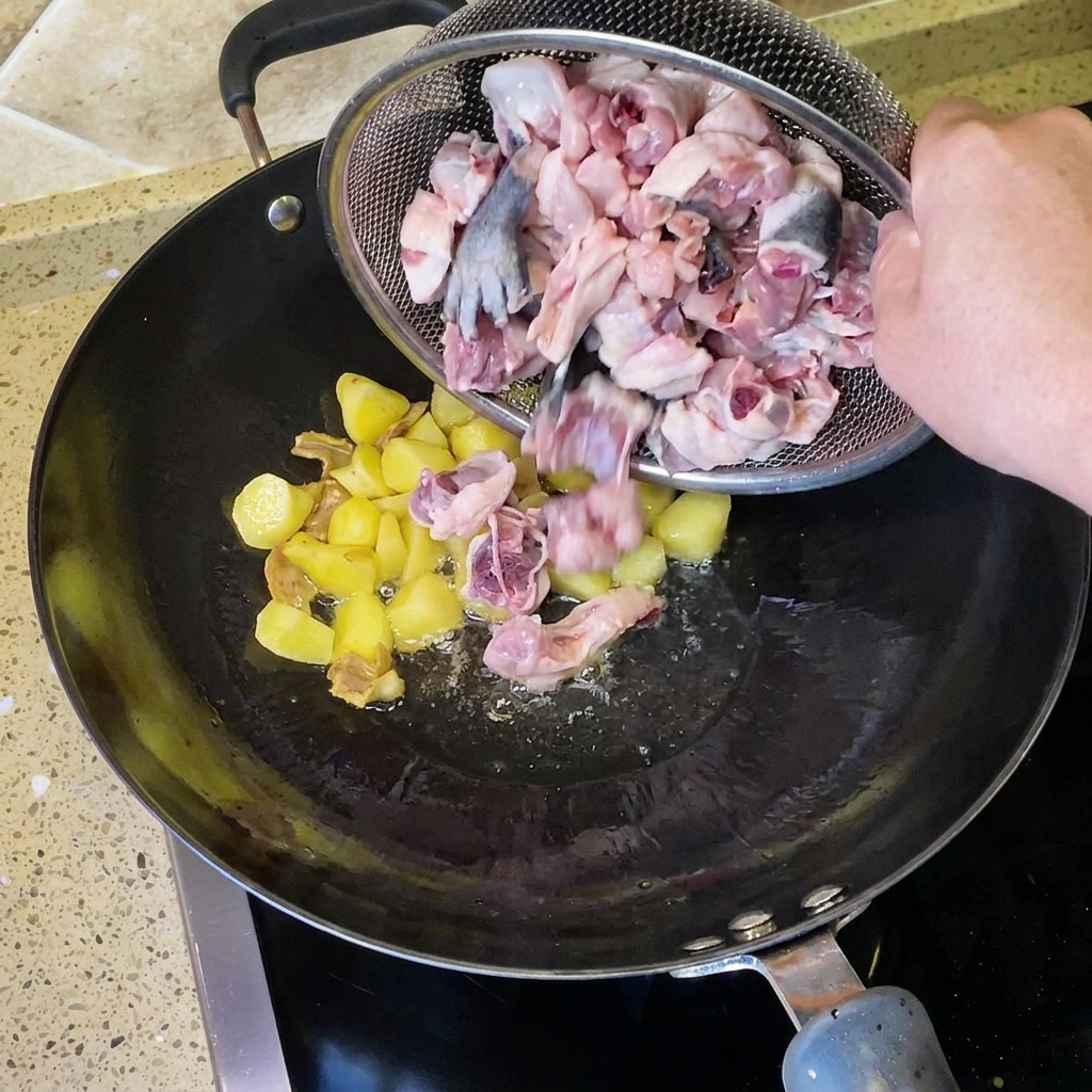 Des morceaux de poulet cru hachés versés dune passoire métallique dans le wok avec les pommes de terre frites et le gingembre.