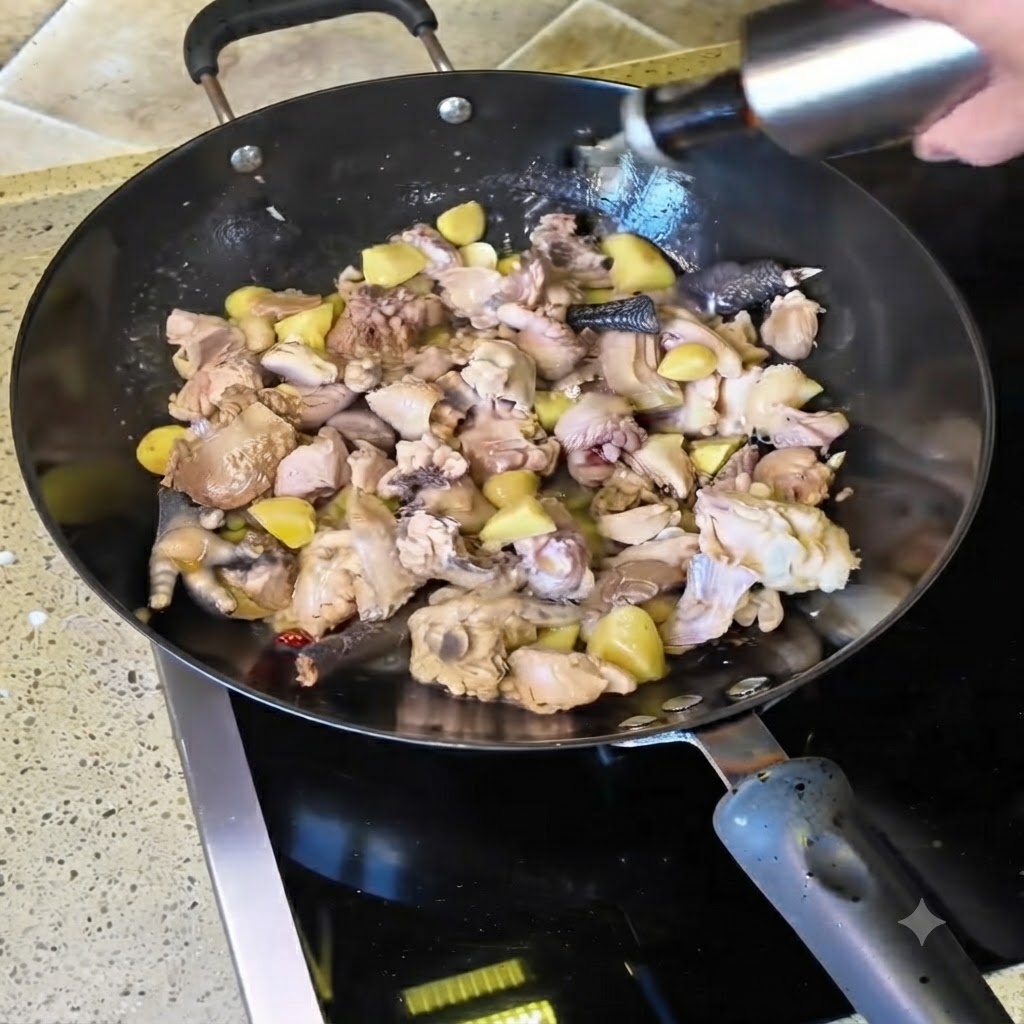 Du vin jaune versé dune bouteille dans le wok rempli de morceaux de poulet sautés.