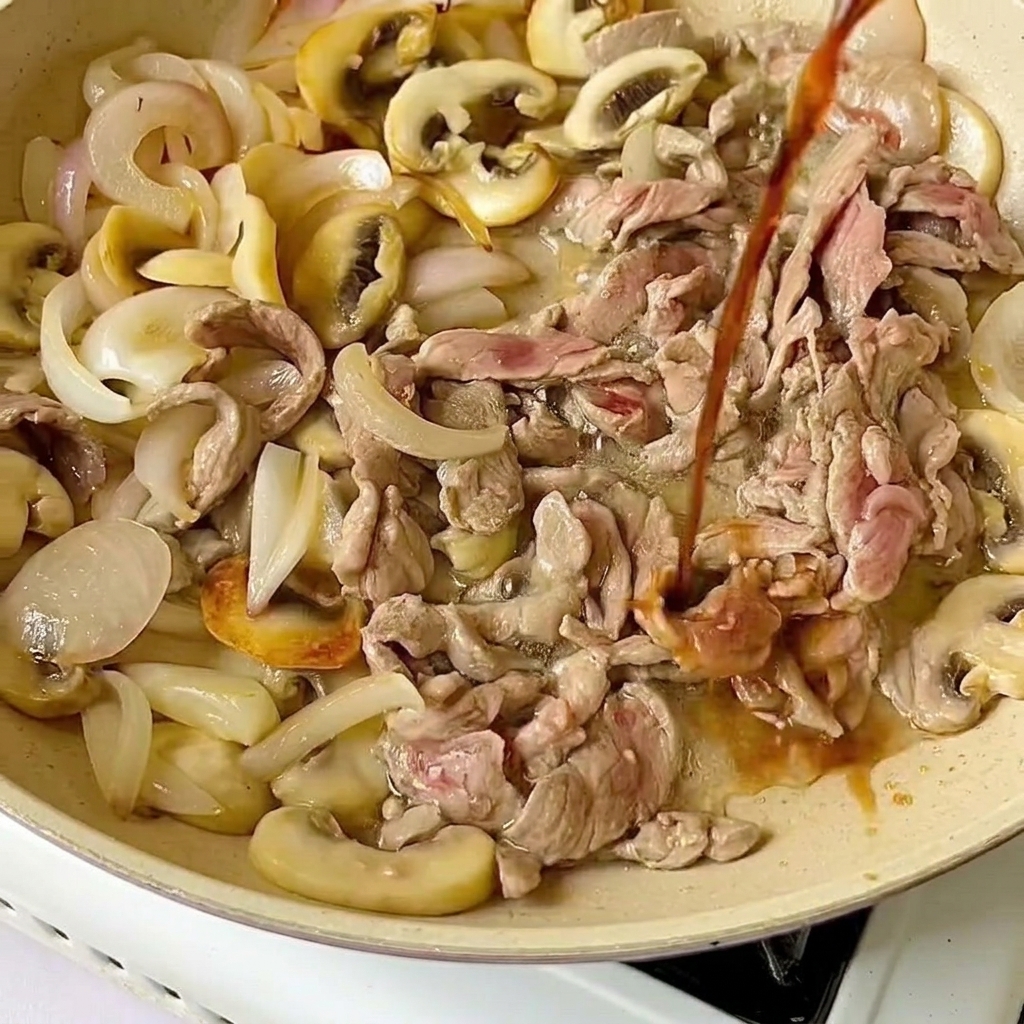 De la sauce soja claire versée du haut sur des tranches de bœuf cru et des légumes cuits dans une poêle.