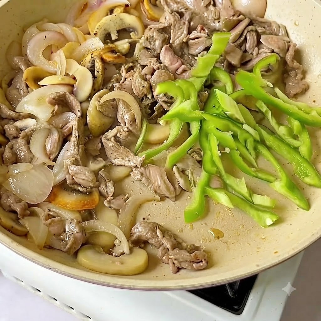 Des tranches de poivron vert frais ajoutées dans la poêle avec le bœuf et les oignons.