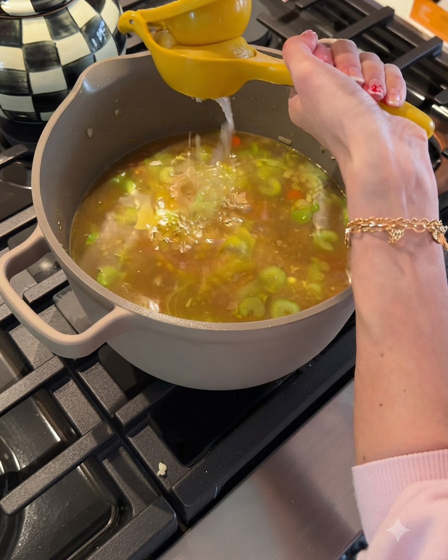 Pressage de jus de citron frais avec un presse-agrumes jaune au-dessus dune marmite de bouillon de poulet et de légumes frémissants.