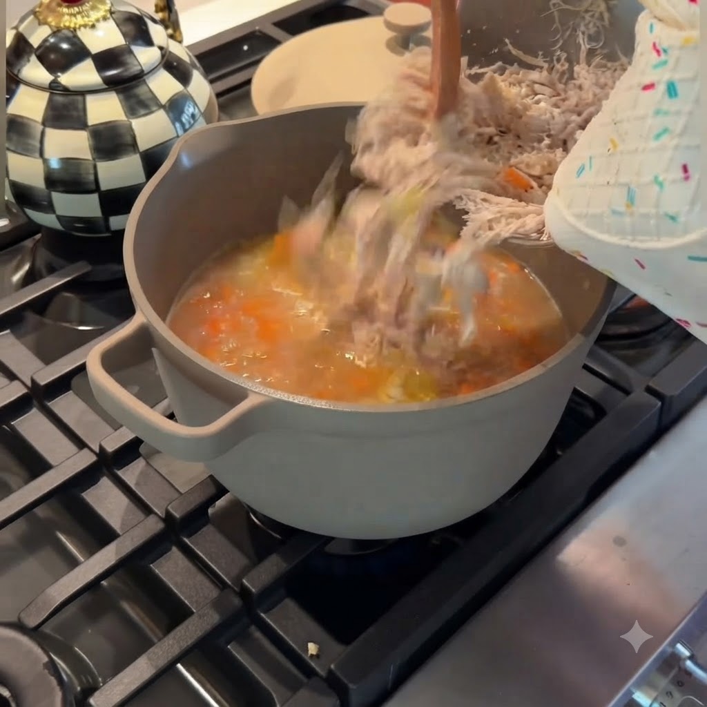 Verser le poulet finement effiloché depuis un bol en métal dans une marmite grise de soupe de poulet et légumes frémissante.