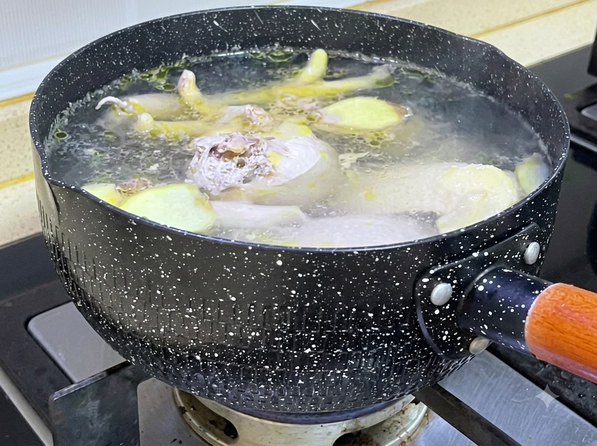 Des morceaux de poulet cru et des tranches de gingembre mijotant dans une casserole noire mouchetée remplie deau bouillante.