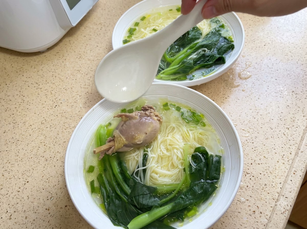 Un bol de nouilles garni dun morceau de poulet et de bok choy cuit.