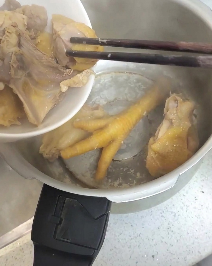 Morceaux de poulet blanchis transférés avec des baguettes dans un autocuiseur en acier inoxydable.