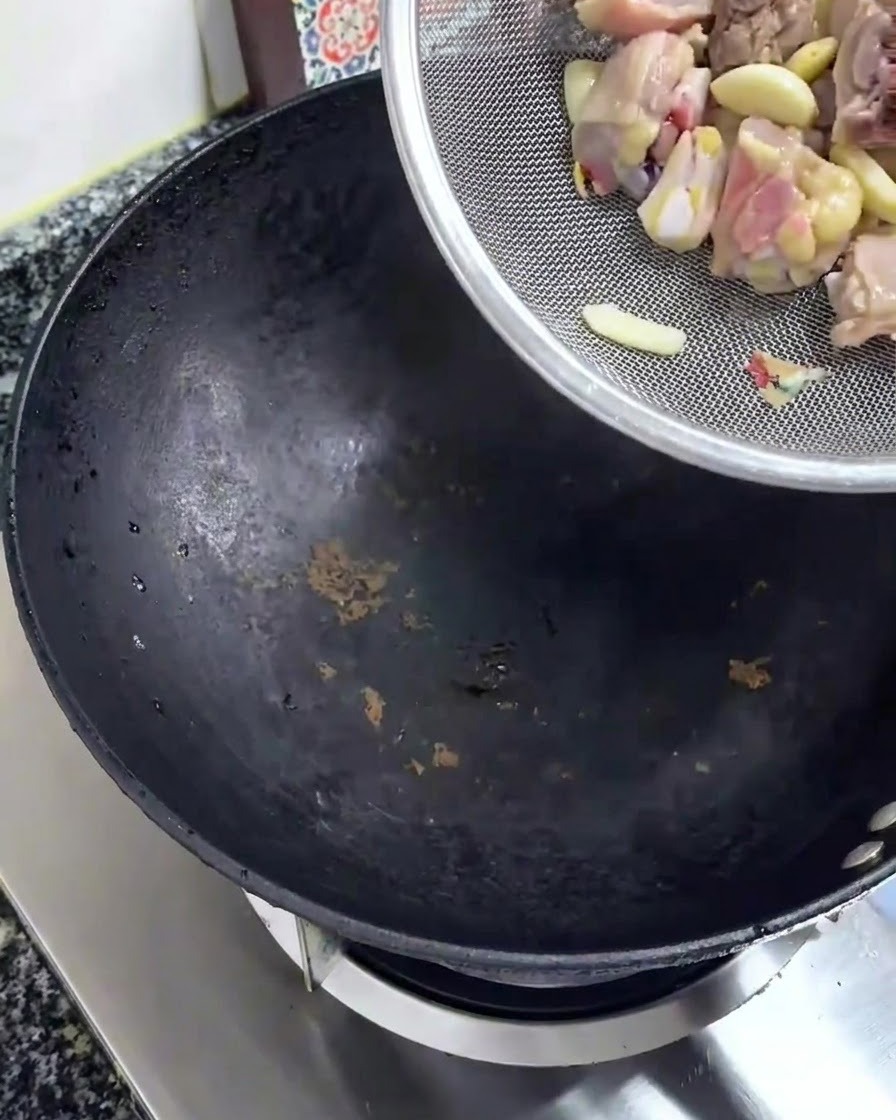 Morceaux de poulet crus et hachés versés dune passoire en argent dans un wok noir.