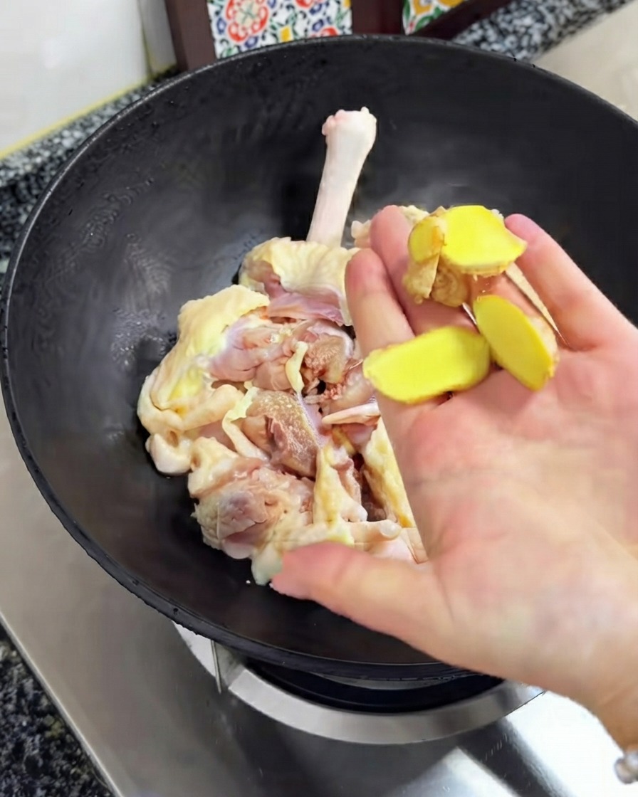 Tranches de gingembre frais tenues au-dessus du poulet cru dans le wok noir.