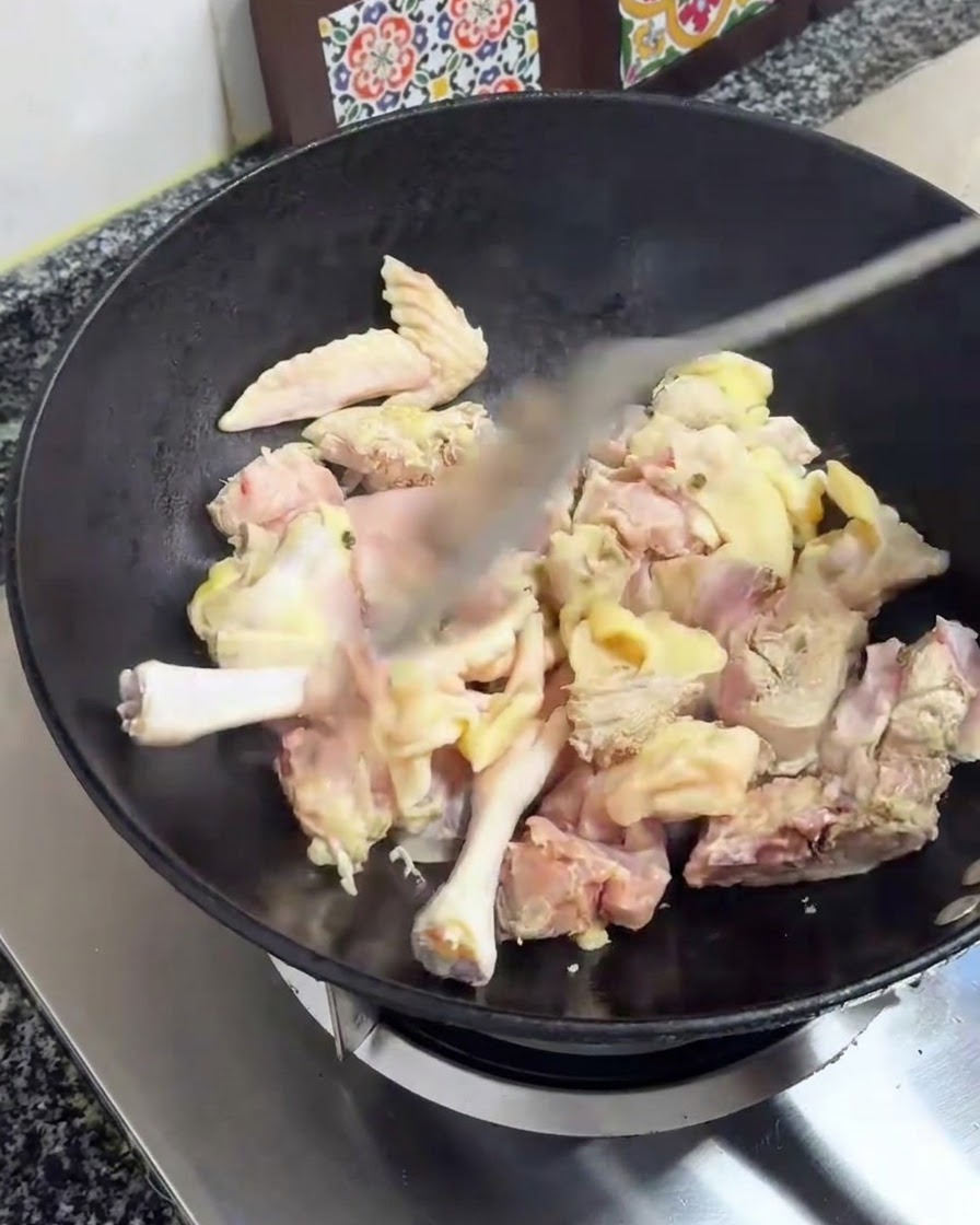 Morceaux de poulet sautés avec une spatule dans un wok noir sur une cuisinière.