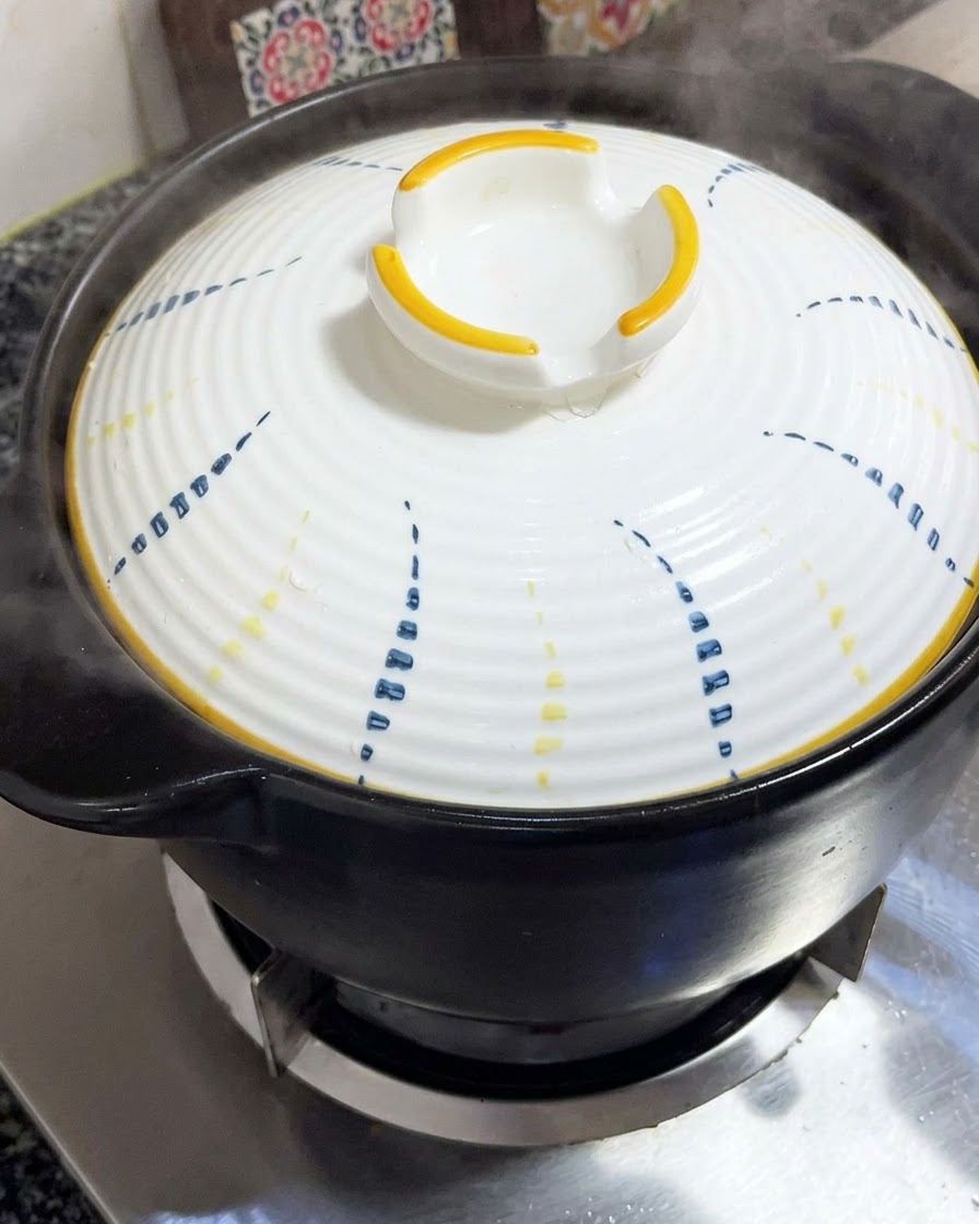 Un couvercle blanc à motifs bleus et jaunes placé fermement sur une cocotte en terre cuite noire.
