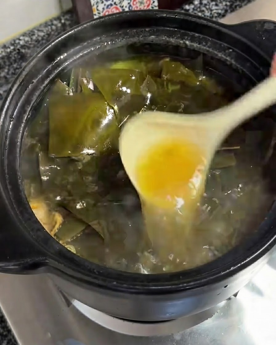 Une louche retirant une couche dhuile jaunâtre de la surface bouillonnante de la soupe.