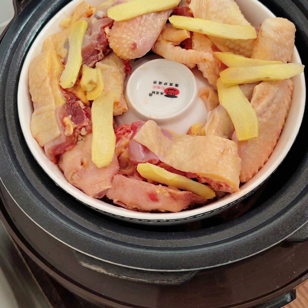 Tranches de gingembre frais déposées sur les morceaux de poulet à lintérieur de la marmite.