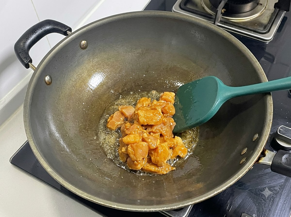 Dés de blanc de poulet mariné sautés dans un wok chaud avec une spatule verte.