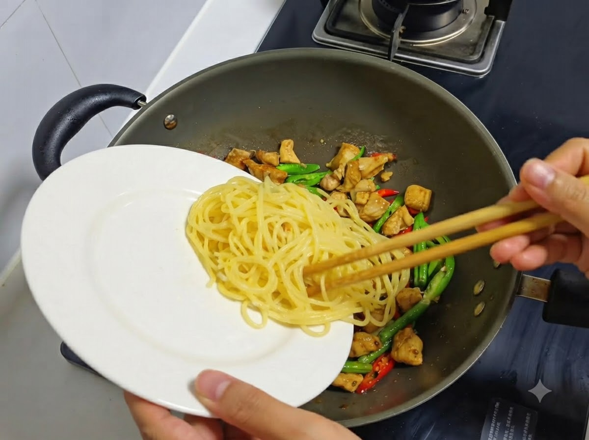 Spaghetti cuits transférés dune assiette blanche dans un wok contenant le poulet et les piments.
