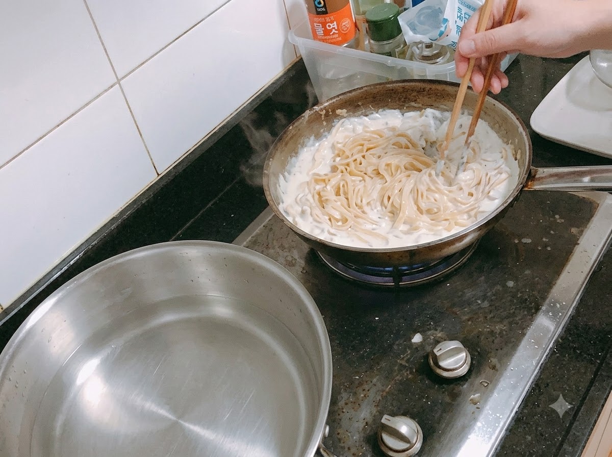 Des pâtes mélangées à la sauce frémissante dans une poêle à laide de baguettes.